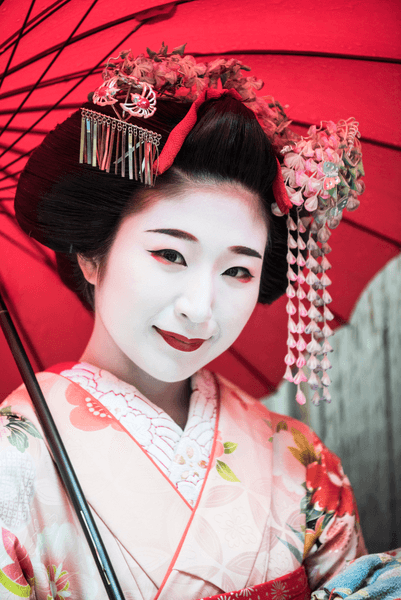 Young Japanese maiko woman with hair accessories and traditional make up smiling towards camera
