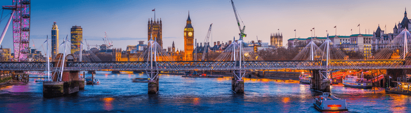 Panoramic view across the landmarks of central London, from the Southbank across the River Thames to the iconic towers of the Houses of Parliament and Big Ben illuminated against the blue dusk sky of the UK's vibrant capital city.