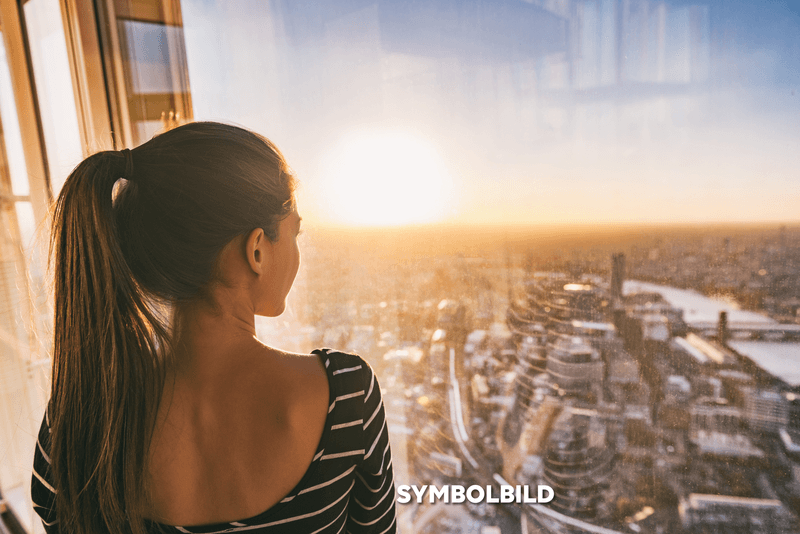 Europe travel woman looking at sunset view of London city skyline from the window of highrise skyscraper tower, famous tourist attraction in the U.K.