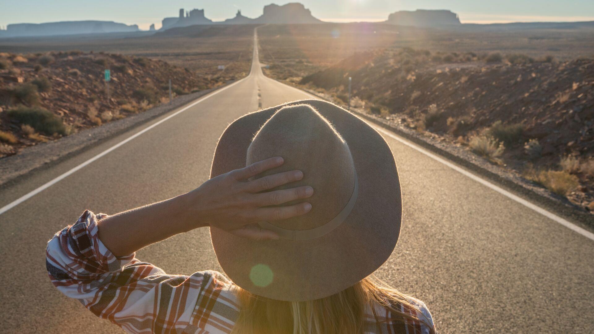 Rear view of woman standing on long highway road leading to Monument Valley in USA. People travel America concept